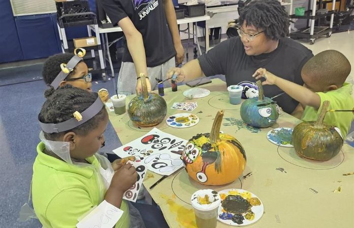   Students sitting around lunch tables painting pumpkins